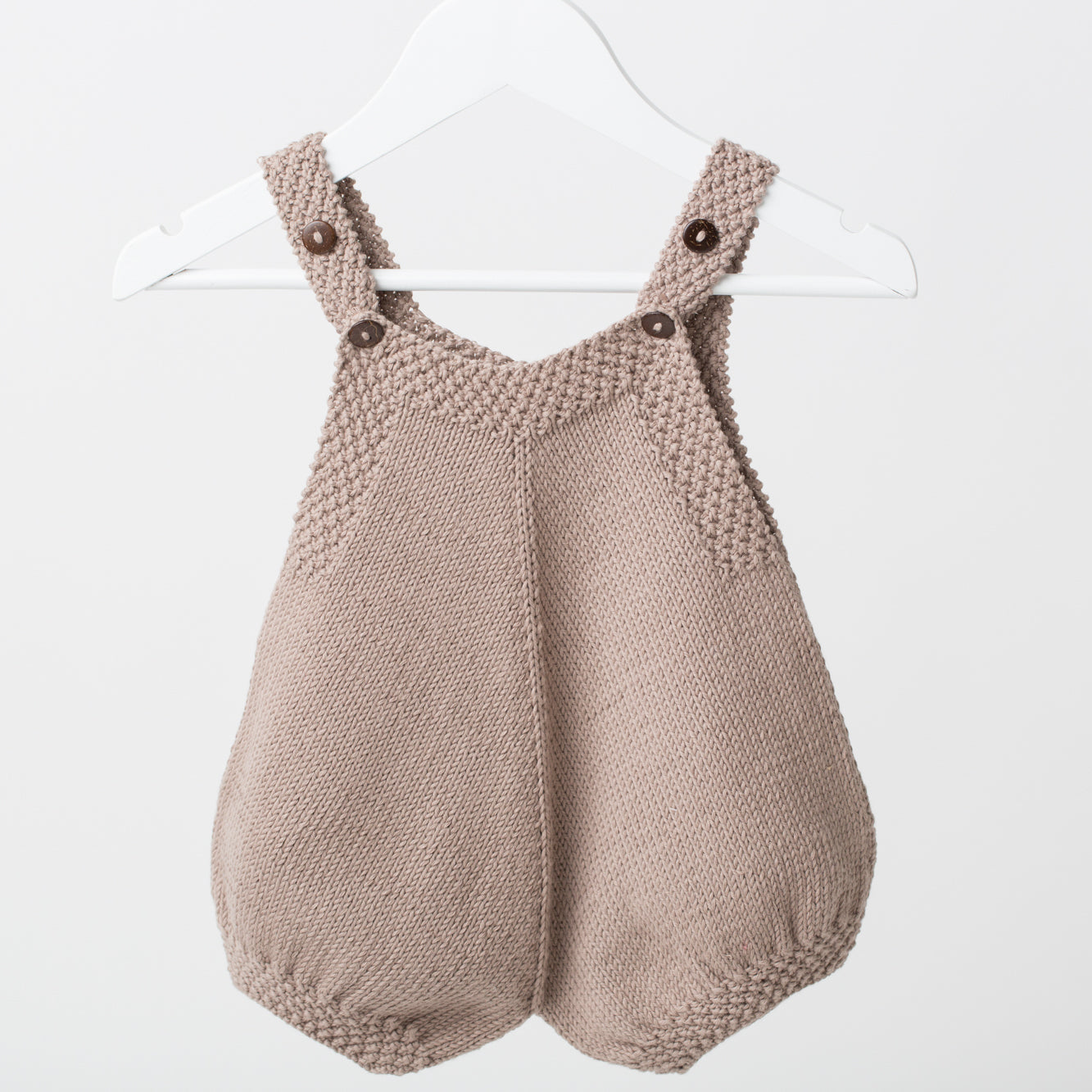 Finn Baby Romper in beige displayed on a hanger, featuring hand-knitted cotton yarn, wooden buttons, and a unique chunky look for newborns.
